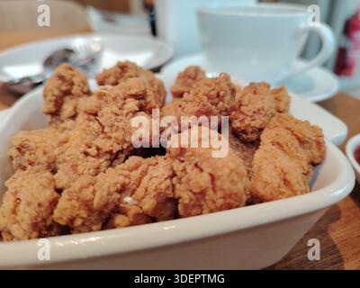 Poulet popcorn frit croquant dans un bol blanc, servi sur une table de café avec un fond de tasse de café flou. Banque D'Images
