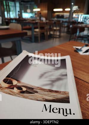 Un menu de restaurant élégant sur une table en bois, avec un intérieur de café flou avec un éclairage ambiant chaleureux. Banque D'Images