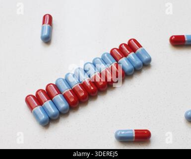 Pilules disposées dans une rangée et d'autres dispersées sur une table blanche, vue de dessus plate, concept médical et de soins de santé avec un fond minimal propre. Banque D'Images