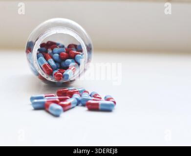 Photo de capsules rouges et bleues dispersées sur une table blanche, avec la bouteille visible en arrière-plan, concept médical et de soins de santé. Banque D'Images
