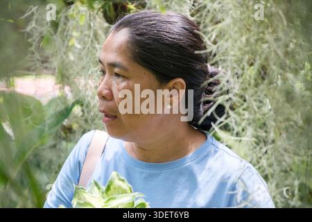 Une femme se déplace dans un jardin rempli de plantes vertes et de mousse suspendue. Elle regarde autour, en prenant dans les vues et les sons de la nature pendant un ensoleillé Banque D'Images