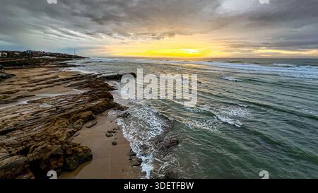 Coucher de soleil sur la mer sur la plage d'Asilah où les vagues de l'océan s'écrasent contre les rochers Banque D'Images
