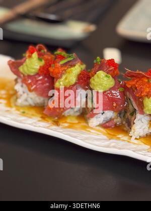 Gros plan d'un rouleau de sushi au thon coloré garni d'œufs, de wasabi et de microgreens, servi sur un plat rectangulaire en céramique. Banque D'Images