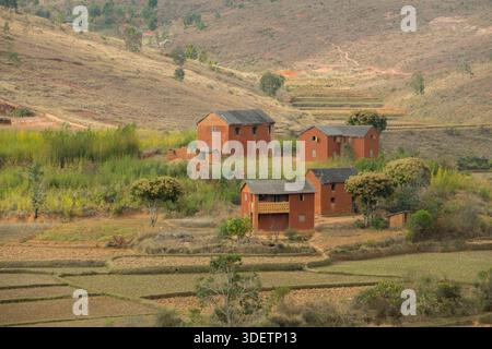 Architecture traditionnelle de village dans les hauts plateaux du centre de Madagascar au sud d'Antananarivo, près de Behenjy sur la N7. Dans les hauts plateaux du centre de Madagascar, en particulier dans les régions au sud d'Antananarivo peuplées par les peuples Merina et Betsileo, l'architecture traditionnelle du village comprend souvent des maisons de deux étages avec un grenier (ce qui en fait essentiellement trois étages), un design connu localement sous le nom de 'Trano Gasy' ('maison malgache'). Les briques d'argile rouge cuites sont le matériau standard, surtout depuis le XIXe siècle. La fa ADE est souvent enduite d'un mélange de terre moulue et de bouse de zébu. Banque D'Images