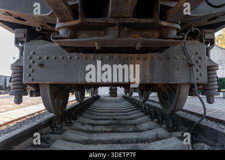 Vue rapprochée des roues de train et du système de suspension du dessous, mettant en évidence les détails industriels et les voies ferrées pour les thèmes des transports. Banque D'Images