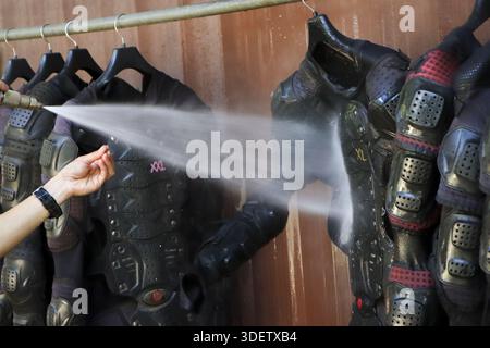 Travailleur énergique pulvérisant l'eau nettoyant costume d'armure futuriste accroché sur le rack, préparant costume noir avec un entretien soigneux, lavant l'équipement sale o Banque D'Images