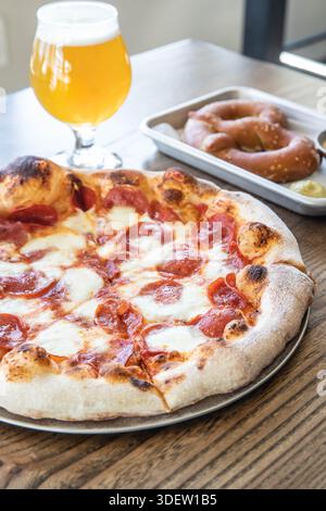 Pizza pepperoni, bière et bretzel sur table en bois Banque D'Images