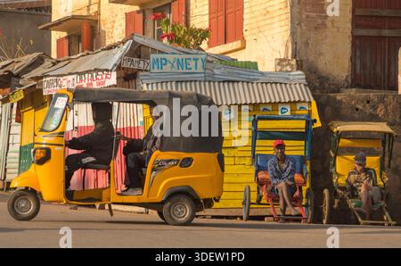 Un pousse-pousse motorisé (tuk tuk) dans la rue. Ces véhicules constituent un mode de transport clé à Ambositra, Madagascar. Ces véhicules sont devenus un élément populaire et essentiel de la vie urbaine dans les grandes villes malgaches, aux côtés des pousse-pousse traditionnels (pousse-pousse à la main ou pousse-pousse à vélo). Ils sont plus rapides et plus à l'aise que leurs homologues à propulsion humaine et fournissent une source vitale de revenus pour les conducteurs de la vaste économie informelle du pays. Ambositra, Madagascar. Banque D'Images