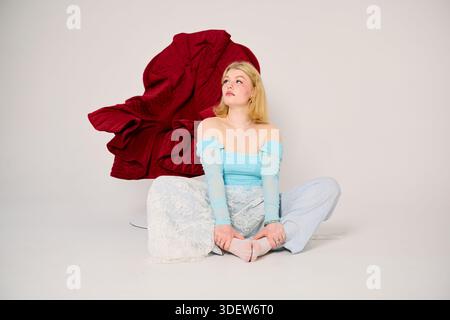 Jeune femme assise sur le sol dans un studio avec un fond rouge Banque D'Images