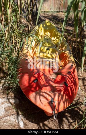 Kayak rouge et jaune tiré entre des roseaux de bambou sur le sable à la lumière du soleil et à l'ombre à Ibiza, Espagne Banque D'Images