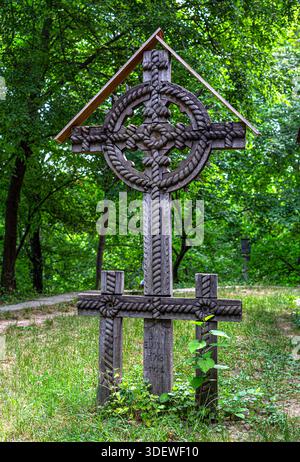 Croix celtique en bois sculptée à la main ornée debout dans un cimetière forestier vert Banque D'Images
