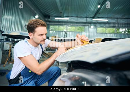 Homme en uniforme faisant réparation de carrosserie de voiture à l'aide d'un outil spécial dans le garage Banque D'Images