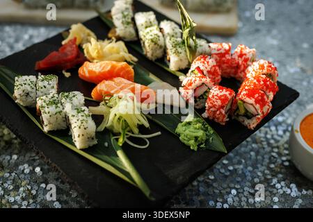 Plateau de sushi assorti avec nigiri, rouleaux, wasabi et garnitures disposés sur un plateau de service sombre. Banque D'Images