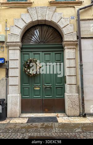 Vieille porte verte en bois dans un closeup de mur de pierre avec une couronne de Noël. Décorations de Noël dans les rues. Vérone, Italie Banque D'Images