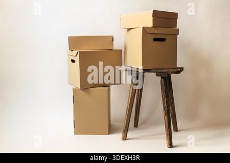 Boîtes et colis en carton sur un vieux tabouret et au sol en différentes tailles, sur fond beige clair, concept de cadeaux de Noël, emballage et expédition, espace copie, focus sélectionné Banque D'Images