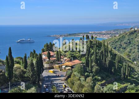 Côte de Taormine avec un bateau de croisière dans la mer bleue et des bâtiments sur les collines Banque D'Images