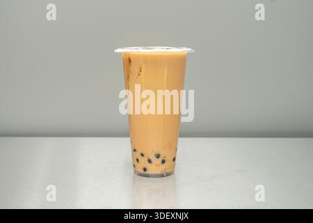 Un gros plan extrême de perles de tapioca noir brillant empilées au fond d'un verre, vu à travers le liquide ambré du thé au lait thaïlandais Banque D'Images