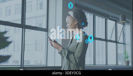 Tenant le téléphone, femme portant un chemisier vert et bandeau vérifiant les messages au bureau avec le code binaire Banque D'Images