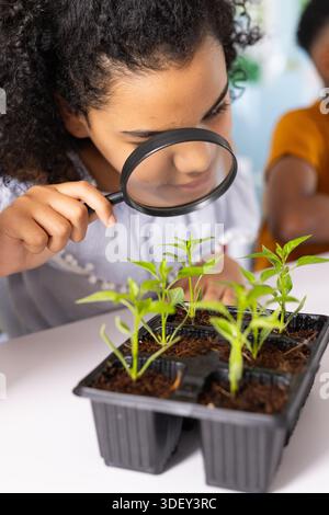 Enfants afro-américains penchés sur le plateau à graines inspectant les germes avec loupe sur le bureau en classe Banque D'Images