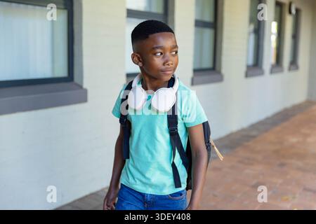 Enfant afro-américain marchant à l'école, portant une chemise à la menthe, un sac à dos noir et des écouteurs blancs Banque D'Images