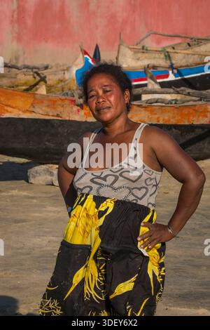 Femme malgache de Morombe sur la plage et attendant de l'aider à décharger les prises du jour des pêcheurs revenant dans leurs canoës à balancier. Dans la ville côtière de Morombe, plaque tournante du peuple Vezo dans le sud-ouest de Madagascar, le rythme quotidien de la vie tourne autour de la mer. La scène d’une femme sur la plage, attendant les pêcheurs de retour dans leurs pirogues, est une représentation intemporelle de leur économie de pêche communautaire. Banque D'Images