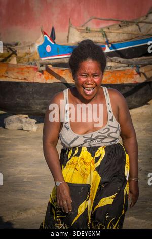 Une femme malgache de Morombe au rire sur la plage et attendant de l'aider à décharger les prises de la journée des pêcheurs revenant dans leurs canoës à stabilisateur. Dans la ville côtière de Morombe, plaque tournante du peuple Vezo dans le sud-ouest de Madagascar, le rythme quotidien de la vie tourne autour de la mer. La scène d’une femme sur la plage, attendant les pêcheurs de retour dans leurs pirogues, est une représentation intemporelle de leur économie de pêche communautaire. Banque D'Images