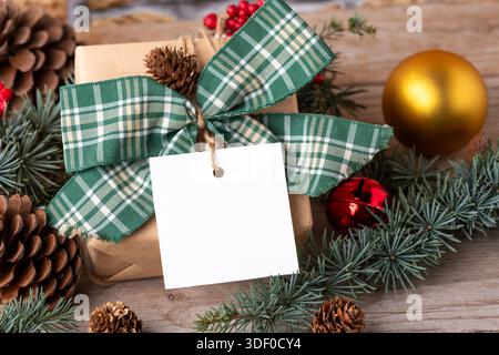 Cadeau de Noël avec étiquette cadeau carrée en papier sur une table blanche avec branches et décorations en sapin vue du dessus.Composition rustique en hiver avec Banque D'Images