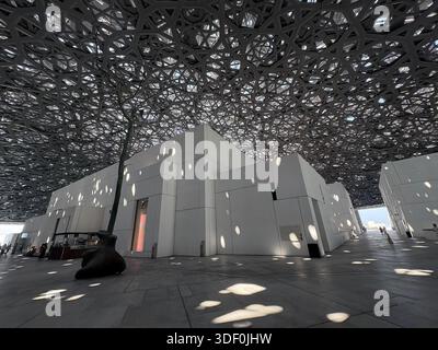 Le dôme emblématique du Louvre Abu Dhabi jette une pluie de lumière fascinante sur sa cour sereine Banque D'Images
