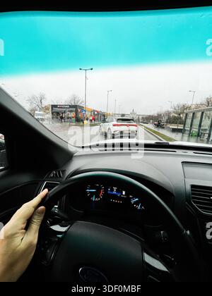 Lviv, Ukraine - 29 novembre 2025 : point de vue du conducteur sur une rue urbaine humide, une voiture devant et des vitrines bordant la route à Lviv, en Ukraine. Banque D'Images
