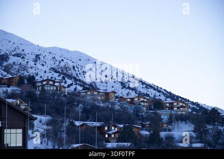 Village de montagne et chalets de villégiature sur une colline enneigée près de la station de ski Amirsoy, région de Tachkent, Ouzbékistan. Destination de voyage d'hiver dans les montagnes Banque D'Images