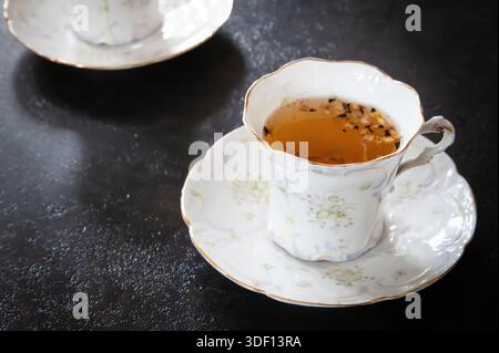 Thé avec des feuilles de thé dedans, dans une tasse à thé sur une soucoupe sur une table en pierre sombre Banque D'Images