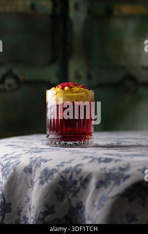 Cocktail rouge avec mousse jaune et poudre de framboise. Banque D'Images