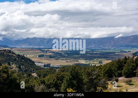 Une vue panoramique sur une vallée luxuriante entourée de montagnes sous un ciel nuageux. Le paysage présente un mélange de verdure et de champs agricoles, avec un Banque D'Images