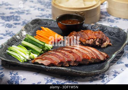 Canard laqué traditionnel servi avec des tranches de concombre, des oignons verts et de la sauce hoisin, stylisé pour un festin élégant. Banque D'Images