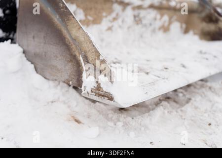 Lame de coupe métallique usée du godet de la chargeuse de chantier capturée dans les moindres détails lors du déneigement sur un chantier par temps froid Banque D'Images