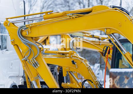 Bras hydrauliques jaunes des pelles hydrauliques de construction lourde avec flexibles et joints visibles garés à l'extérieur dans des conditions hivernales montrant des machines industrielles Banque D'Images