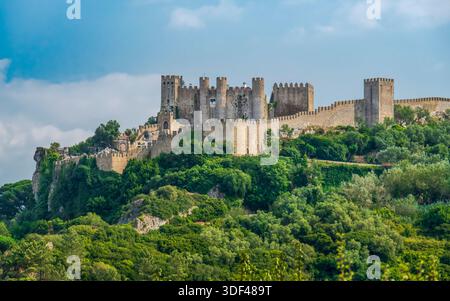 Château d'Obidos sur une colline surplombant une forêt verdoyante au Portugal, murs de pierre médiévale s'élevant au-dessus du paysage sous un ciel lumineux et h intemporel Banque D'Images