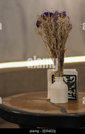 Bouquet séché compact dans un vase bouteille blanc avec des serviettes sur une table de café rustique. Banque D'Images