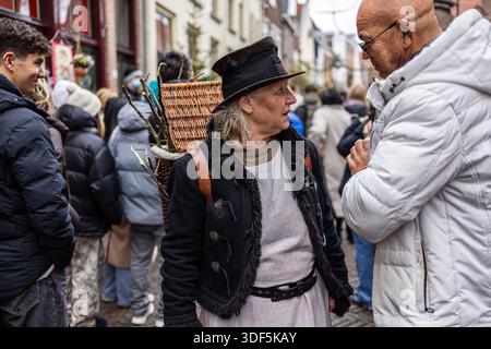 Deventer, Overijssel, pays-Bas - 14.12.2025, au Festival Charles Dickens. Femme plus âgée en manteau noir et bonnet avec panier en osier parle à l'homme Banque D'Images