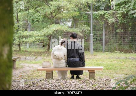 Couple portant un kimono et un yukata assis sur un banc dans un parc verdoyant. Kyoto, Japon. Banque D'Images