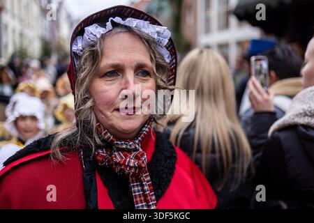 Deventer, Overijssel, pays-Bas - 14.12.2025, au Festival Charles Dickens. Femme en manteau rouge et bonnet en dentelle se dresse dans la foule festive, habillée f Banque D'Images