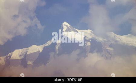 Montagne enneigée s'élevant au-dessus des nuages sous un ciel bleu, créant un paysage alpin dramatique et serein. Banque D'Images