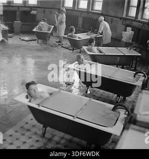 Slaviansk, RSS d'Ukraine, années 1970 Un grand plan historique représente une séance de balnéothérapie dans le sanatorium de la célèbre station balnéaire de Slavkurort. Plusieurs patients masculins se détendent dans des baignoires individuelles remplies d'eau minérale thérapeutique dans un hall carrelé spacieux. Des assistantes médicales en uniforme de coton blanc surveillent la procédure. De grandes fenêtres éclairent la pièce. Cette authentique photographie d'archives monochrome capture l'atmosphère du tourisme de santé soviétique et les pratiques curatives dans la paisible région du Donbass Banque D'Images