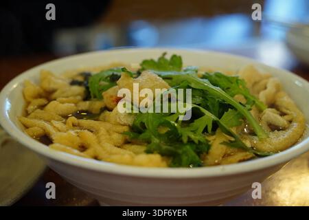 Délicieuse soupe de nouilles udon de style coréen avec des légumes verts dans un bol blanc, gros plan Banque D'Images