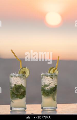 Deux cocktails mojito sur une table en gros plan sur la plage, sur fond de soleil couchant au coucher du soleil, sable et mer. Vacances dans le sud chaud Banque D'Images