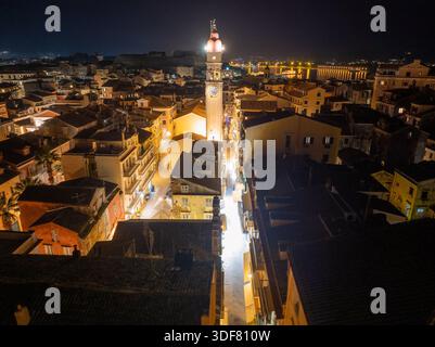 Vue verticale aérienne du clocher illuminé de l'église Saint Spyridon s'élevant au-dessus des toits sombres de la vieille ville de Corfou pendant la nuit de Pâques Banque D'Images