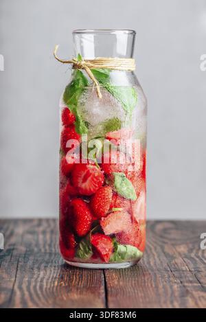 Eau détox en bouteille avec des feuilles de fraise fraîche et de basilic. Orientation verticale Banque D'Images