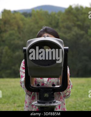 Fille regarde directement la caméra à travers une paire de jumelles publiques géantes dans un parc Banque D'Images