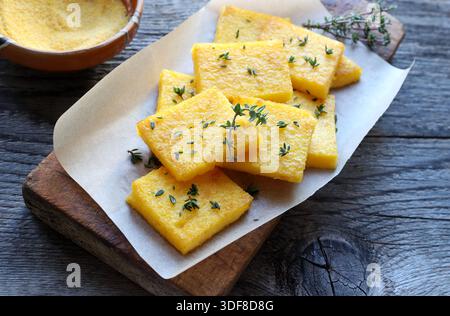 Un plat de polenta ou de copeaux de polenta, tranché ​​and frit ou cuit au four, assaisonné de thym frais. Fabriqué à partir de semoule de maïs et d'eau. Vue de dessus. Cuisine italienne. Banque D'Images