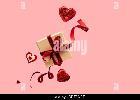 Boîte cadeau avec ruban rouge et coeurs sur fond rose pour la célébration de la Saint-Valentin Banque D'Images